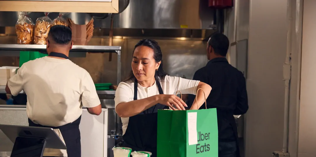 Uber Eats clone app development — restaurant kitchen staff preparing food orders with branded Uber Eats delivery bag